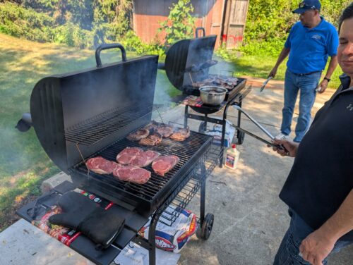 Two guys grilling steaks at company picnic